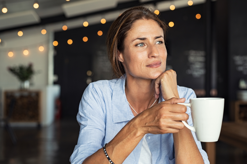 Thoughtful,Mature,Woman,Sitting,In,Cafeteria,Holding,Coffee,Mug,While