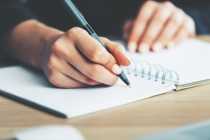 Close,Up,Of,Woman's,Hands,Writing,In,Spiral,Notepad,Placed