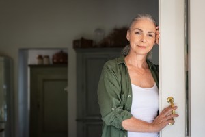 Portrait,Of,Senior,Woman,Leaning,Against,Door,At,Home,And