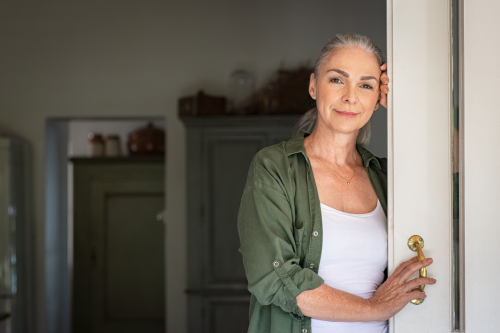 Portrait,Of,Senior,Woman,Leaning,Against,Door,At,Home,And