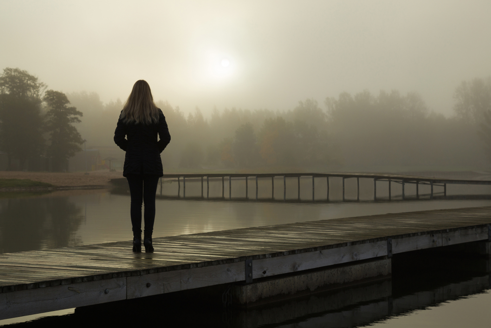 Young,Woman,Standing,Alone,On,Lake,Footbridge,And,Staring,At