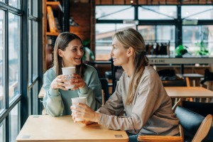 Two,Women,Sitting,In,A,Coffee,House,Talking,And,Drinking